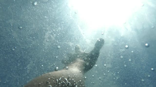Man's hand stretches underwater to surface of the sea. Arm asking for help in air bubbles and trying to survive. Point of view of man, drowning in deep ocean