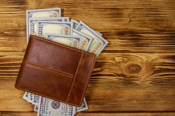 istock Brown leather wallet and american dollars on wooden table. Top view 1128600309