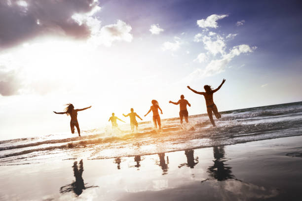 istock Group happy peoples silhouettes run sunset beach 1128608081