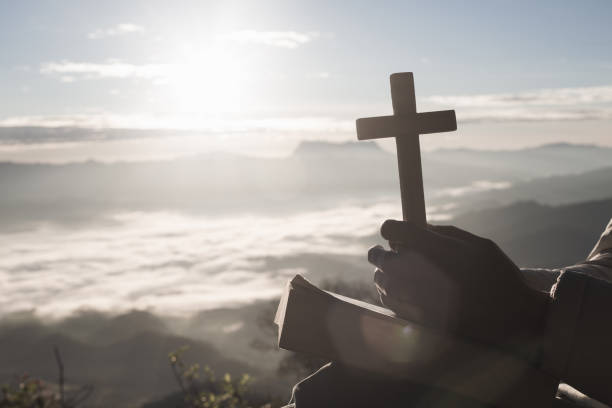woman praying while holding bible and cross, pray in the morning , woman praying with hands together on the sunrise background. - praying human hand worshipper wood imagens e fotografias de stock