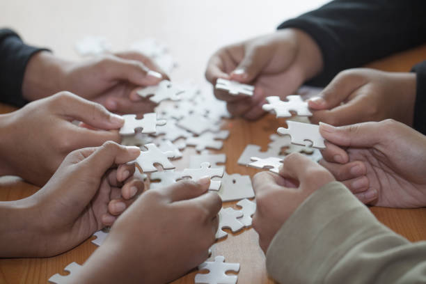istock Hands of diverse people assembling jigsaw puzzle, Youth team put pieces together searching for right match, help support in teamwork to find common solution concept, top close up view 1128622788