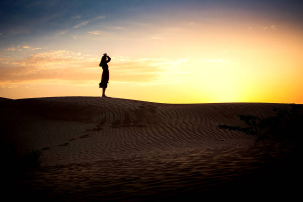 istock Woman watching sunset in a desert silhouette 1128632995