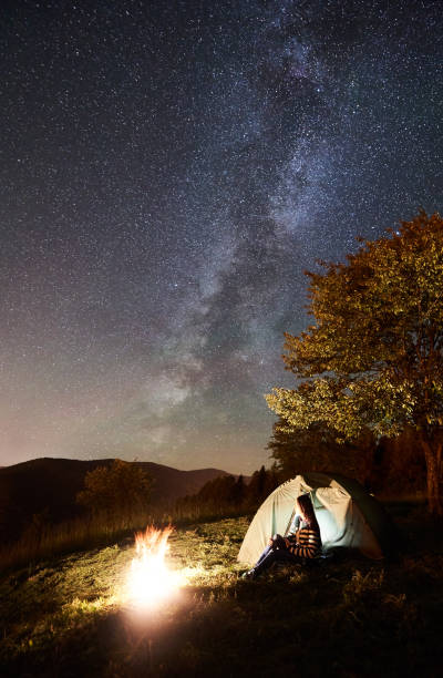 istock Woman resting at camp and tent under under night starry sky 1128633213