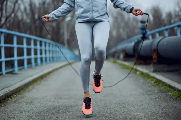 Unrecognizable female athlete exercising with jump rope while having a sports training outdoors.