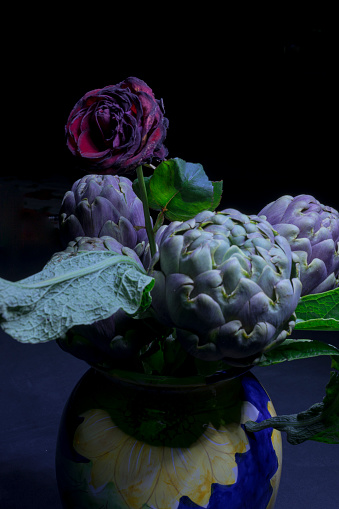 A rose and three artichokes in a blue vase. Night shot in a hand-painted blue ceramic vase with floral motifs.
