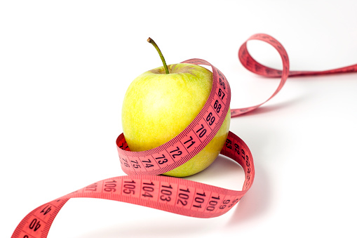 green apple with measuring tape lying on a wooden background