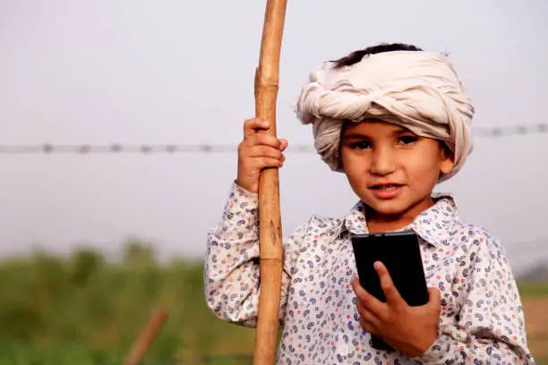 Photo of Cute little child standing near green field holding mobile phone