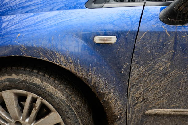 Mud splashes on the side of blue car. Dirty vehicle during rainy weather on road.