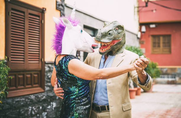 Crazy couple dancing and wearing dinosaur t-rex and unicorn mask - Senior elegant people having fun masked at carnival parade - Absurd, eccentric, surreal, fest and funny masquerade concept Crazy couple dancing and wearing dinosaur t-rex and unicorn mask - Senior elegant people having fun masked at carnival parade - Absurd, eccentric, surreal, fest and funny masquerade concept fashion show photos stock pictures, royalty-free photos & images