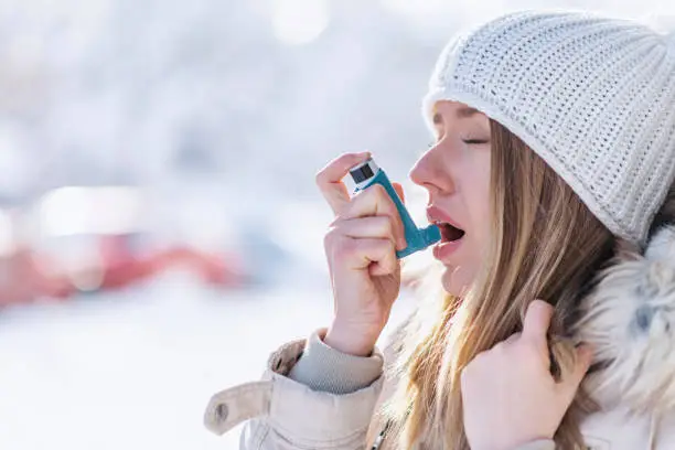 Portrait of a woman using an asthma inhaler in a cold winter. Woman with Inhaler Suffering Asthma Attack in Winter Asthmatic patient managing condition with medication in cold season