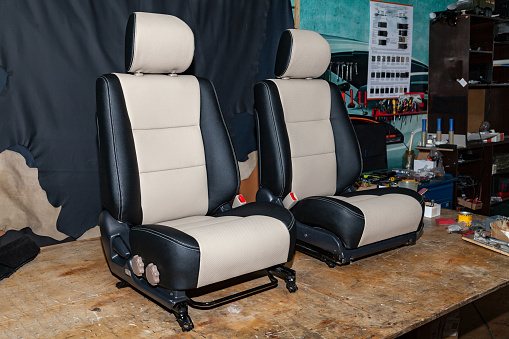 Two front seats with combined leather trim in two colors of black and beige, located on the workbench in the workshop for repair and tuning of cars and vehicles