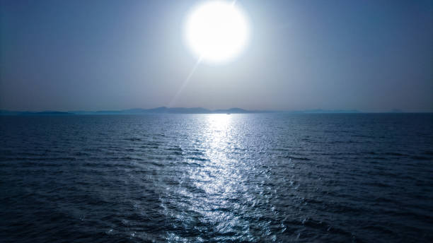 A blue image showing the sea, the horizon and the sun. The sun gets reflected in the water