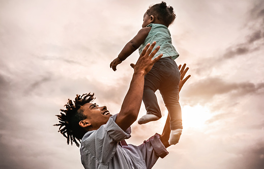 Happy father playing with his baby daughter during sunset time - Afro family having fun outdoor - Concept of child, happiness and parenthood