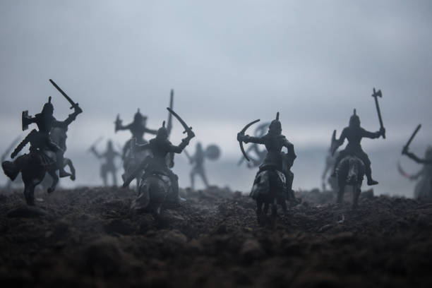 istock Medieval battle scene with cavalry and infantry. Silhouettes of figures as separate objects, fight between warriors on sunset foggy background. Selective focus 1128663726