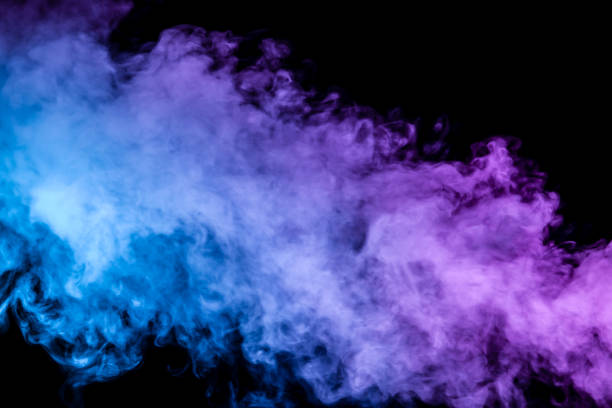 istock Translucent, thick smoke, illuminated by light against a dark background, divided into three colors: blue, green and purple, burns out, evaporating from a steam of vape for T-shirt 1128664625