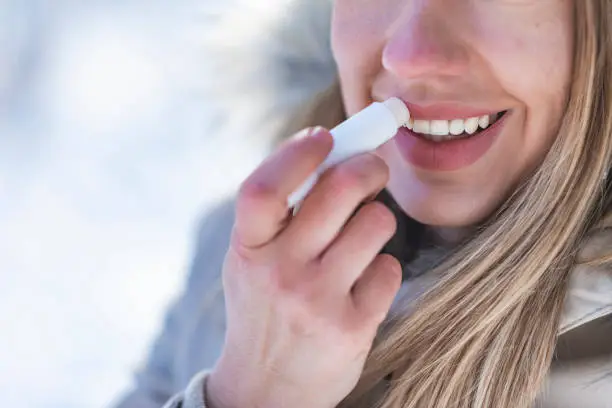 Portrait of young female applying lip balm in winter. Portrait of a beautiful woman in snow with application of the protective cream to the lips