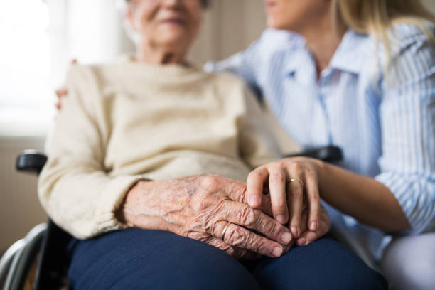 A senior woman in wheelchair with a health visitor at home at Christmas time. Unrecognizable senior woman in wheelchair with a health visitor at home at Christmas time. a helping hand photos stock pictures, royalty-free photos & images