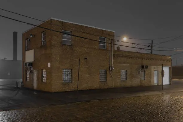 Two story vintage industrial brick building in urban area with streetlight and fog at night