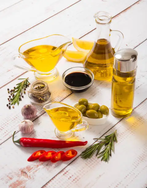 Olive oil in different glass containers on a light wooden table with spices.