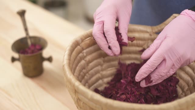 Close-up as a girl gently puts dried rose petals in a copper mortar with pestle.