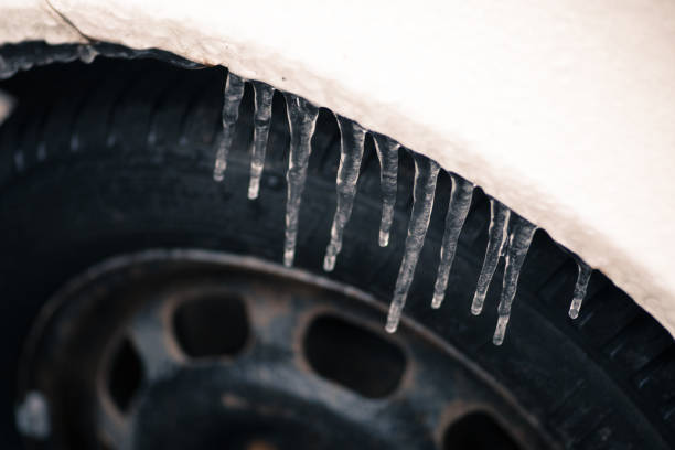 Long icicles hanging at a car with tire show slippery streets after blizzard with extreme low temperature for urban drive problems in winter with the need for car insurance against ice and frosty days