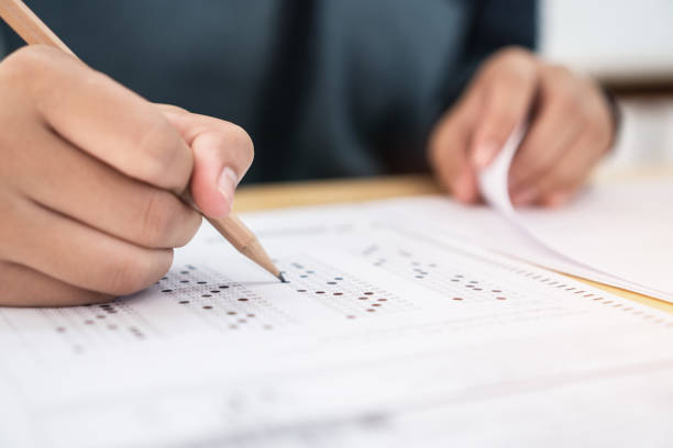 istock Education test exam concept, high school / university student holding pencil writing paper answer sheet on lecture chair for taking exams in examination room or classroom. Educational assessment ideas 1128674808