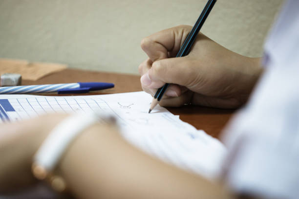 istock Asian Students holding pencil in hand doing multiple-choice quizzes or testing exams answer sheets exercises on old wood table In secondary school, college university classroom in education concept 1128674892