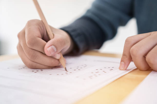 istock Education test exam concept, high school / university student holding pencil writing paper answer sheet on lecture chair for taking exams in examination room or classroom. Educational assessment ideas 1128674901