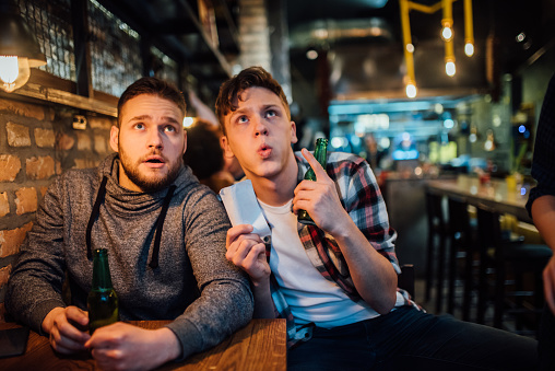 Two young male friends drinking beer and watching game on TV