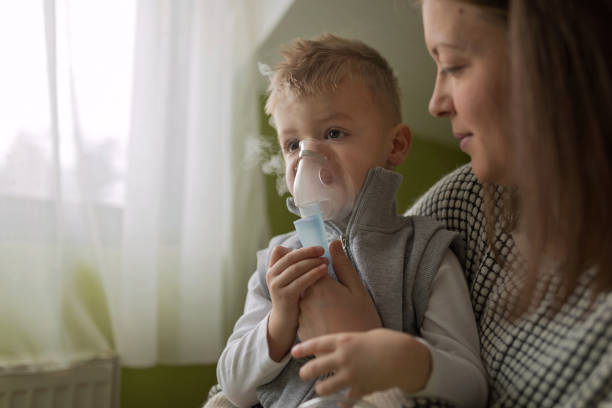 mutter hilft kleinen sohn mit vernebler während des einatmens - asthmatic child asthma inhaler inhaling stock-fotos und bilder