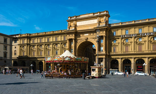 People walking past children riding on the famous carousel in the Piazza della Repubblica, a major town square in the old town section of Florence, Italy.