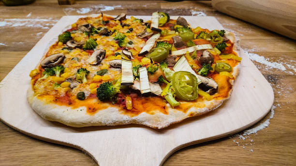 a vegan pizza on a pizza shovel on a wooden table with flour, angled view - pepperoni pizza green olive italian cuisine tomato sauce imagens e fotografias de stock