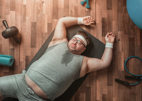 Funny overweight sportsman lying down exhausted on the gym's floor
