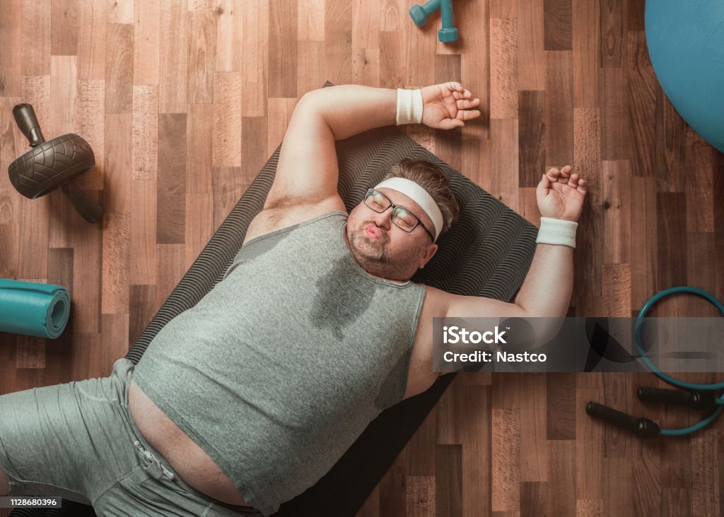 Funny exhausted overweight sportsman Funny overweight sportsman lying down exhausted on the gym's floor Overweight Stock Photo