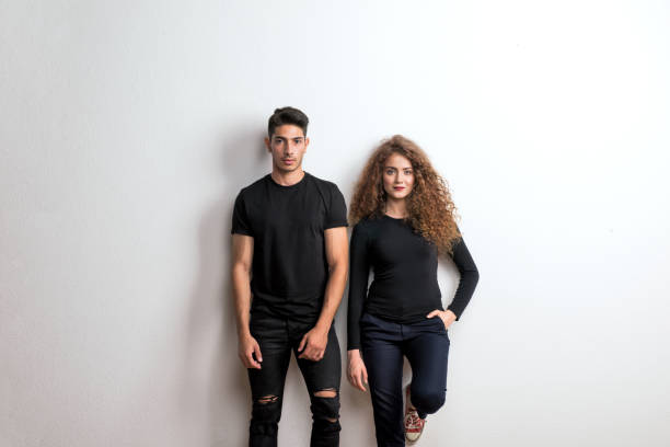 retrato de una joven pareja en un estudio de pie, vistiendo ropa de color negro. - teenager beautiful female men fotografías e imágenes de stock