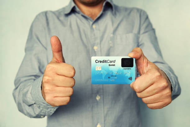 Close up of young man in shirt holding credit card with biometric technology and showing thumb up. Man is glad to use bank card of new type. Advantages of using banking. Biometric payment card. Sign. Close up of young man in shirt holding credit card with biometric technology and showing thumb up. Man is glad to use bank card of new type. Advantages of using banking. Biometric payment card. Sign cvc stock pictures, royalty-free photos & images