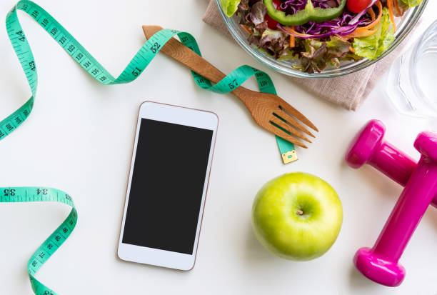 istock Fresh salad with green apple, dumbbell, measuring tape and empty screen smartphone on white background. Diet, healthy eating concept 1128682773