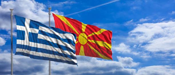 istock Greece and North Macedonia waving flags on blue sky background. 3d illustration 1128684381