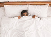 African-american man in bed hiding under blanket