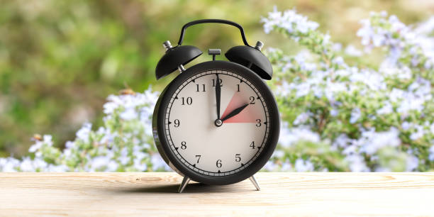 European daylight saving time. Alarm clock on wooden desk, blur spring nature background. 3d illustration stock photo
