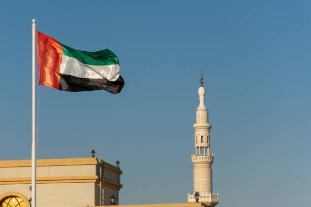 istock UAE Flag blowing in the wind with a mosque minaret and blue sky background. 1128684900