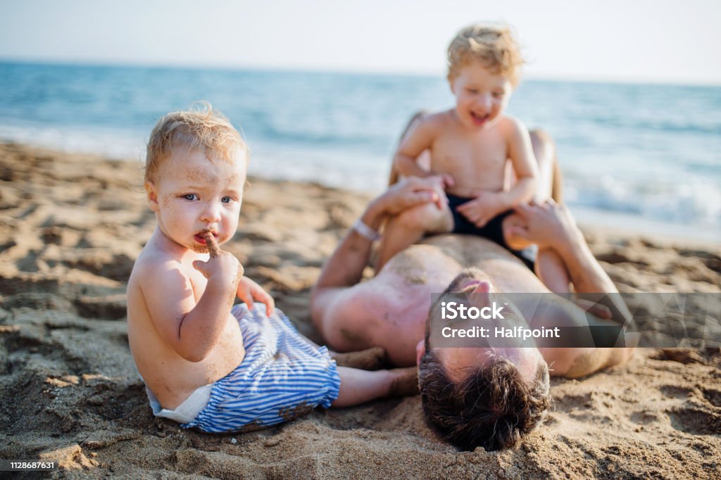 Ein Vater mit zwei Kleinkind Kindern im Sommerurlaub am Sandstrand liegen. - Lizenzfrei Schmutzig Stock-Foto