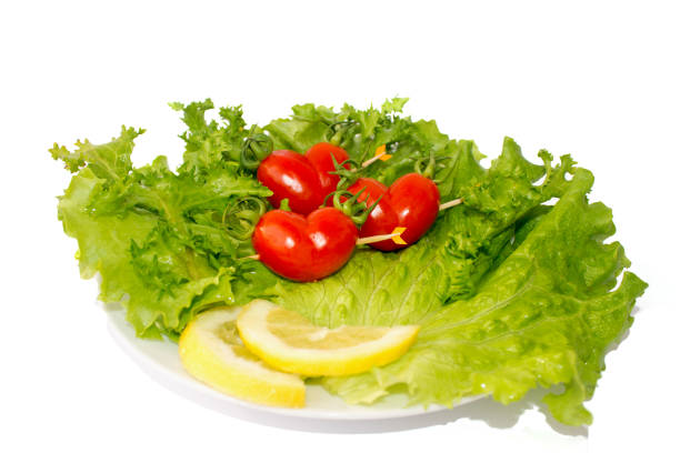 three small red tomatoes cherry on the green iceberg salad and lemon slidce