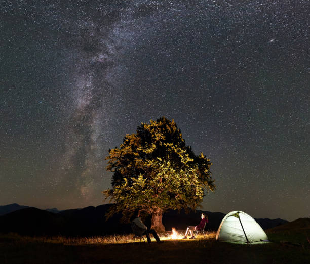 istock Couple tourists at night camp in mountains under starry sky 1128694508