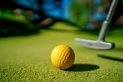 Mini Golf yellow ball with a bat near the hole at sunset
