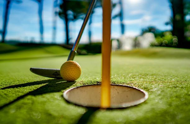 istock Mini Golf yellow ball with a bat near the hole at sunset 1128694813