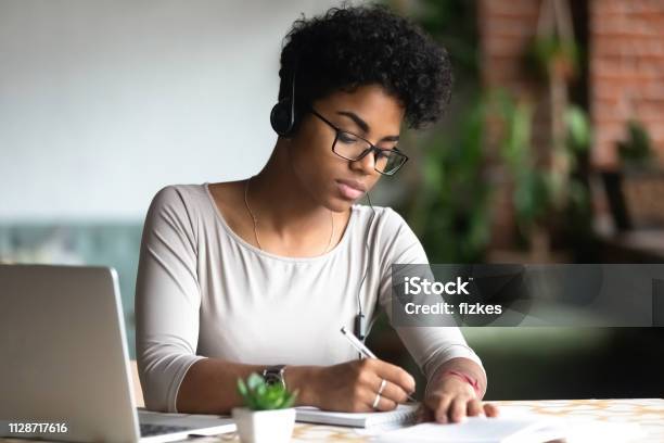 Serious African Woman Studying Using Internet Holding Pen Writing Notes Stock Photo - Download Image Now