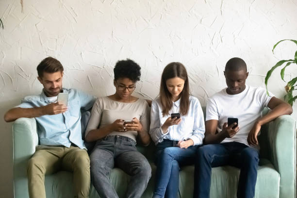 istock Four young people sitting on couch absorbed by smartphones 1128717661