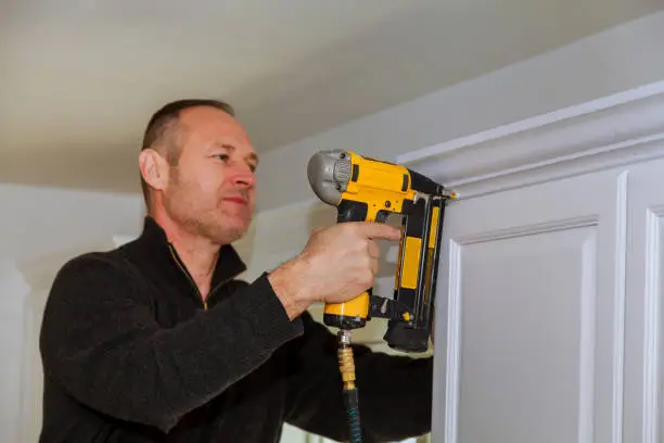 Air Nailer Tool, Carpenter using nail gun to crown moldings on kitchen wall cabinets