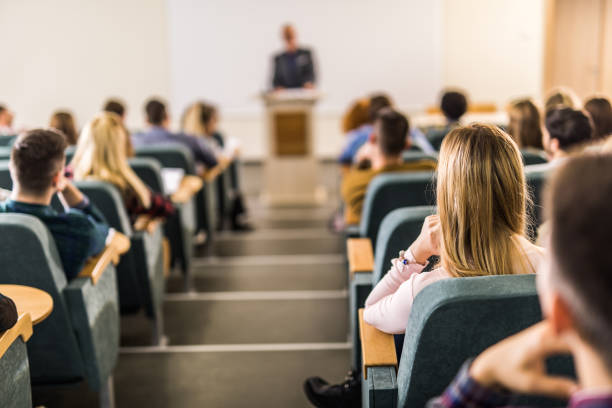 istock Rear view of large group of students on a class at lecture hall. 1128724100